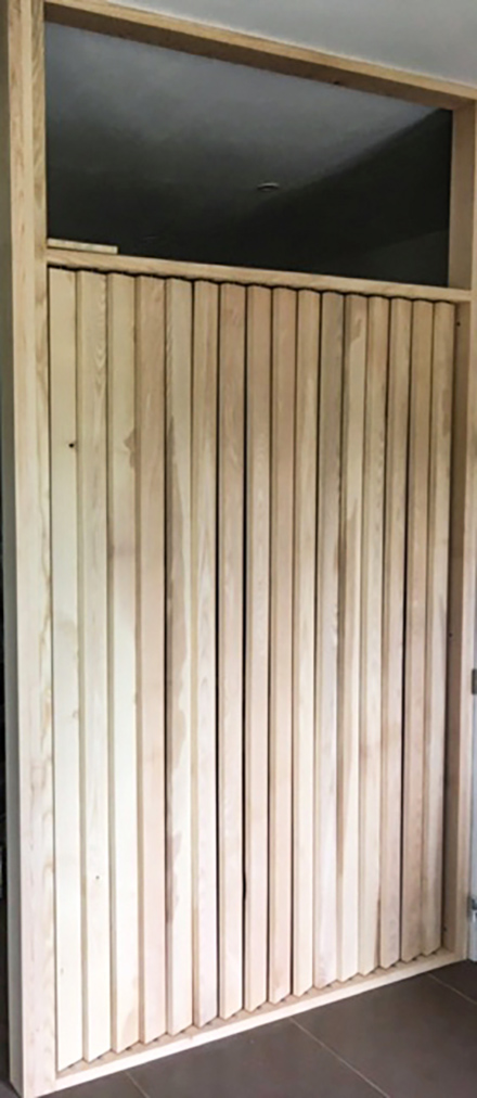 Photo d'une claustra en frêne à persiennes rotatives réalisée pour séparer une pièce en deux.