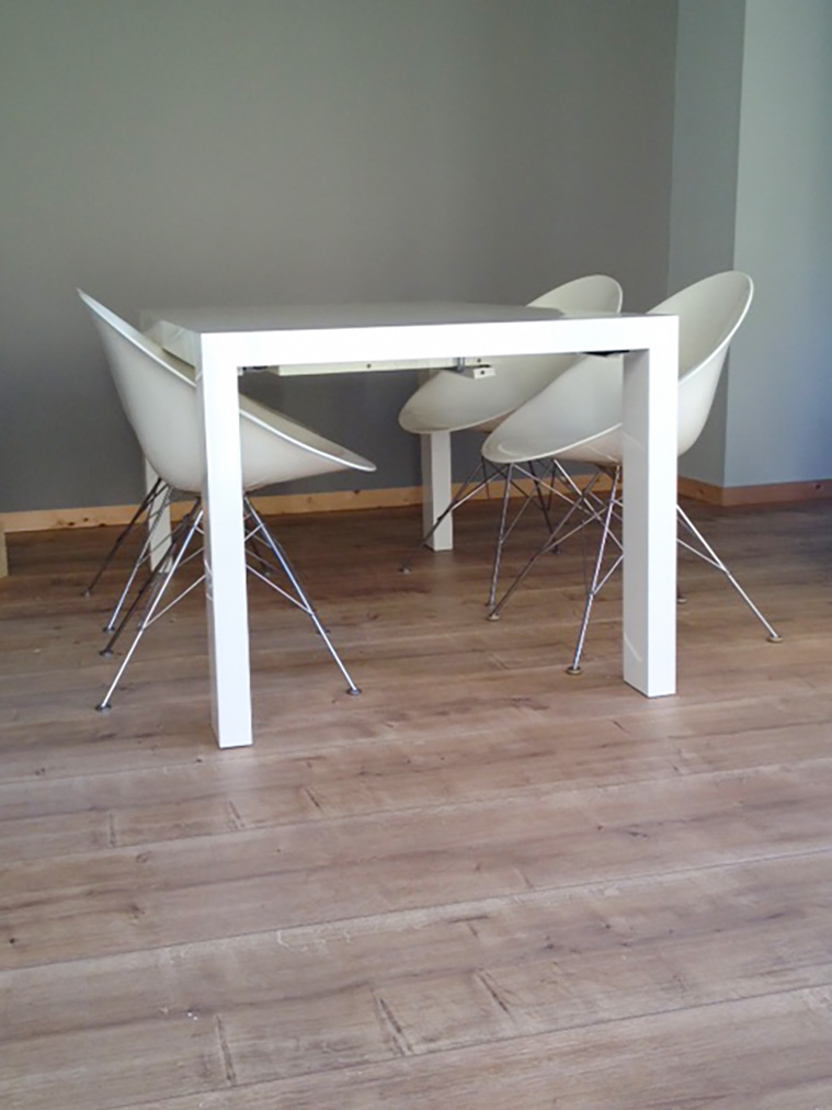 Photo présentant un parquet stratifié et une table carrée laquée blanche avec quatre chaises style Acapulco non ajourées en polyéthylène blanc.