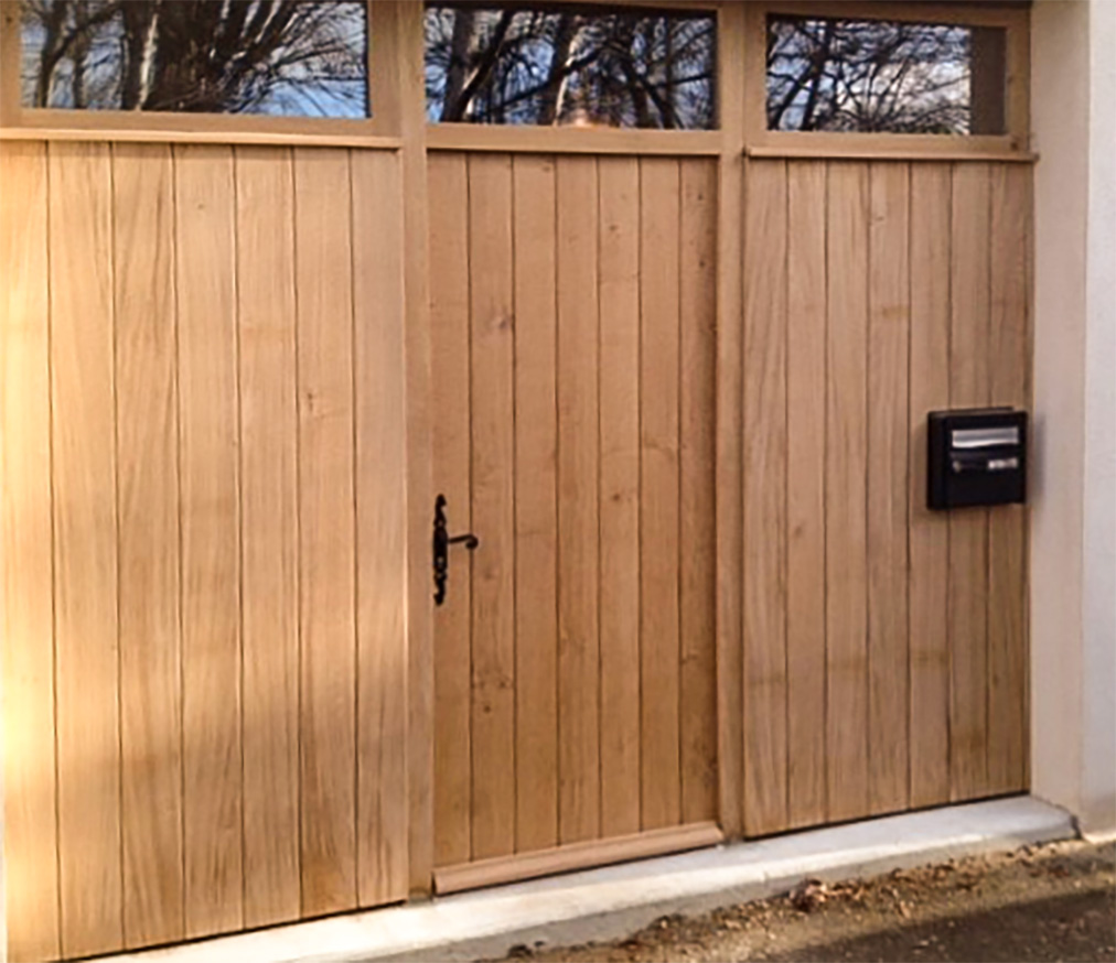 Vue d'une porte de garage transformée en porte d'entrée avec deux panneaux de bois clair de chaque côté.